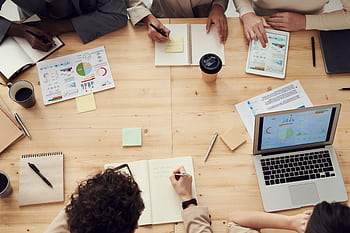 Business professionals in a collaborative team meeting, discussing charts and plans with laptops and notebooks. HD wallpaper