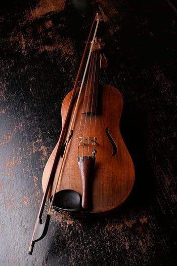 A beautifully crafted violin rests on a dark wooden surface, evoking a classic and artistic mood. HD phone wallpaper