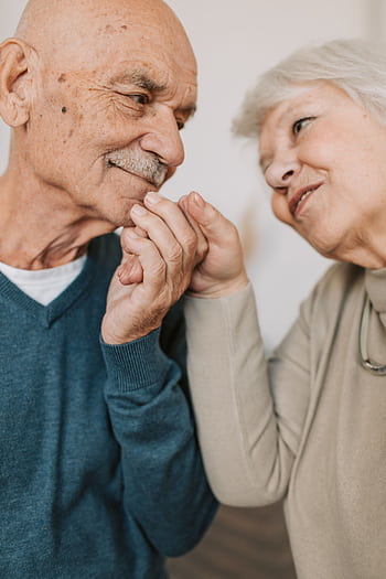 An elderly couple expressing love and affection, holding hands indoors. HD phone wallpaper