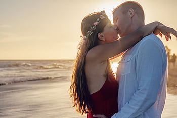 Young couple sharing a romantic kiss on a beach at sunset. HD wallpaper