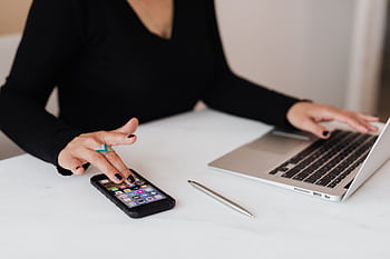 A professional woman multitasking with a smart and laptop at an office desk. HD wallpaper