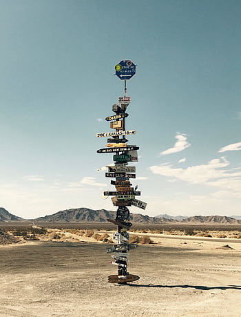 Tall signpost in a desert landscape under a clear blue sky with mountains in the background. HD phone wallpaper
