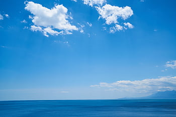 A wide expanse of calm ocean meets the bright blue sky with scattered clouds on a clear day. HD wallpaper