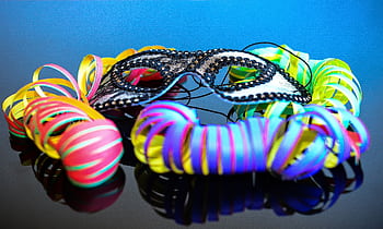 A vibrant close-up of a decorative mask surrounded by colorful streamers on a reflective surface. HD wallpaper