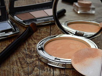 Close-up of makeup tools including compact, brush, and mirror on a rustic wooden surface. HD wallpaper
