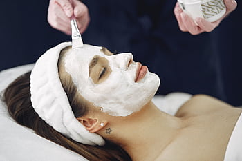 Close-up of a woman with eyes closed enjoying a calming facial mask application at a spa. HD wallpaper