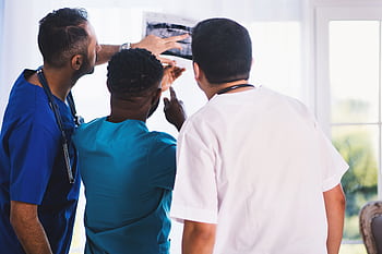 Doctors collaboratively analyzing an X-ray in a clinical setting, showcasing teamwork and medical expertise. HD wallpaper
