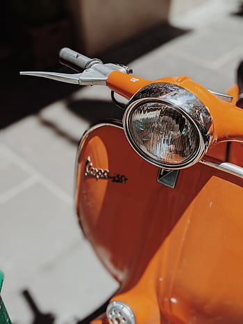 Close-up of a vintage orange Vespa scooter parked outdoors, showcasing its classic design. HD phone wallpaper