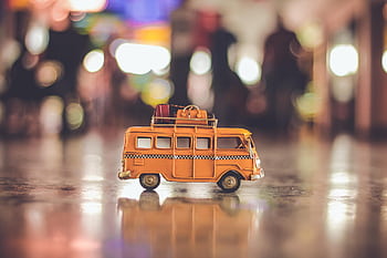 Close-up of a toy yellow campervan with luggage on a reflective surface and blurred lights. HD wallpaper