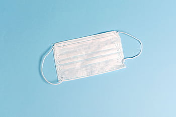 A disposable face mask lying on a light blue surface, symbolizing health protection. HD wallpaper