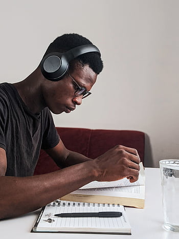 An adult man intensely studying with heads, pen, and notebook at a desk indoors. HD phone wallpaper