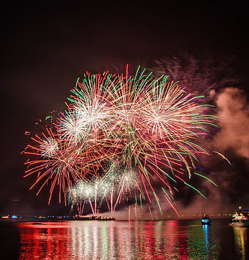 Colorful fireworks illuminating the night sky above a serene water body, creating a festive atmosphere. HD phone wallpaper