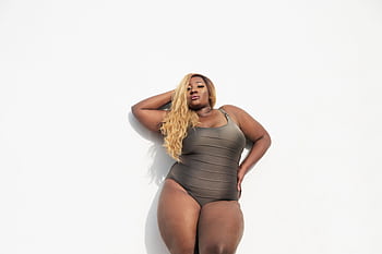A confident black woman in a swimsuit posing against a white background, embracing body positivity and fashion. HD wallpaper