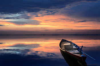 A serene scene of a wooden boat floating on a calm sea at sunset, reflecting vibrant colors and a tranquil atmosphere. HD wallpaper