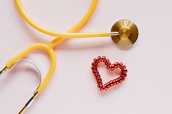 A yellow stethoscope and red heart decoration symbolize love and healthcare on soft pink. HD wallpaper