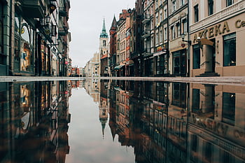 A tranquil street in Toruń, Poland, with historic architecture reflecting in a puddle. HD wallpaper