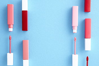 Colorful lip gloss tubes laid out on a bright blue background, showcasing modern cosmetics. HD wallpaper