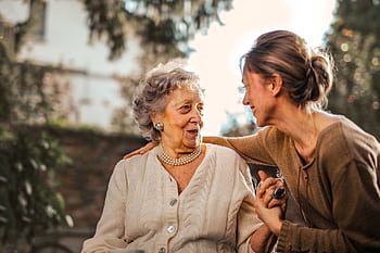 Elderly woman and adult daughter share a joyful, affectionate moment in a sunny garden. HD wallpaper