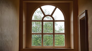 An elegant arched window design framing a lush green view of trees outside. Interior shot. HD wallpaper