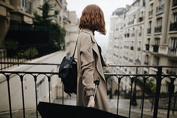 Woman in trench coat walking through a Parisian street with an umbrella, showcasing city life and travel. HD wallpaper