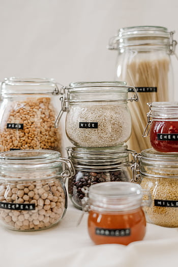 Glass jars filled with diverse kitchen ingredients like rice and chickpeas on a white background. HD phone wallpaper