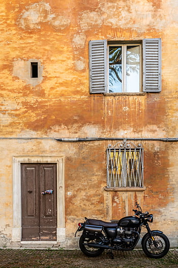 A classic motorcycle parked by a weathered wall in Urbino, Italy, showcasing timeless architecture. HD phone wallpaper