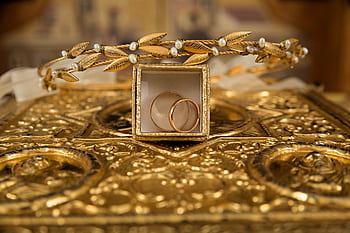 Close-up of gold wedding rings and a delicate tiara on an ornate golden background, symbolizing luxury and elegance. HD wallpaper