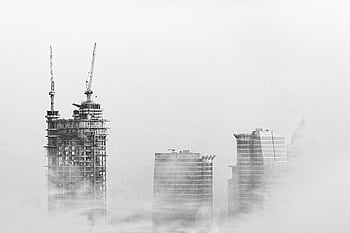 Black and white of Dubai skyline with skyscrapers and cranes emerging from fog, showcasing urban development. HD wallpaper