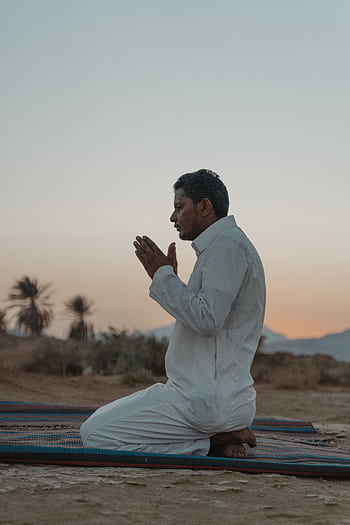 A man kneeling in prayer at sunset outdoors, embracing religious traditions. HD phone wallpaper