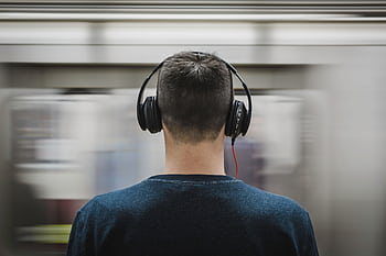 Rear view of a man with heads standing at a subway platform, blurred train passing by. HD wallpaper