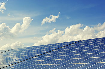 Sleek modern solar panels under a vibrant blue sky with clouds, symbolizing clean energy. HD wallpaper