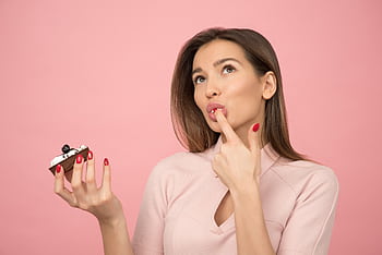 A young woman with long hair savoring a tasty cupcake, posing against a pink background. HD wallpaper