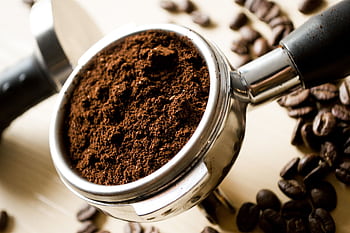 Close-up of freshly ground coffee in a portafilter with scattered coffee beans. HD wallpaper