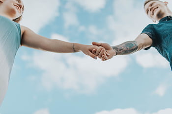 A couple holds hands outdoors, symbolizing love and connection, graphed from a low angle. HD wallpaper
