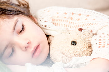 Peaceful child cuddling a teddy bear while sleeping, exuding warmth and security. HD wallpaper