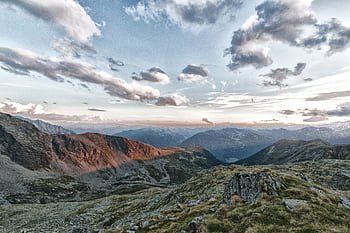 Scenic view of a majestic mountain range with rocky formations and clouds at sunset. HD wallpaper