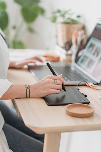 A woman working on a graphic design project using a tablet and laptop in a modern office. HD phone wallpaper