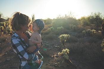 A mother holding her baby in a desert landscape at sunset, surrounded by cacti. HD wallpaper