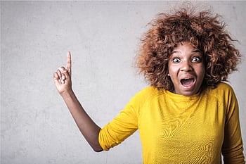 Portrait of a joyful woman pointing upwards, expressing excitement in a studio setting. HD wallpaper