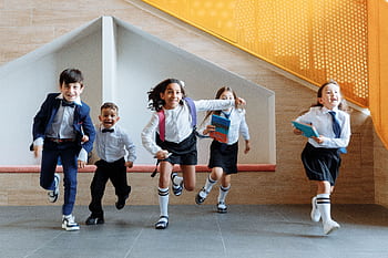 Happy school children in uniforms running energetically indoors, expressing excitement. HD wallpaper