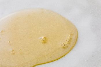 Close-up of a golden liquid with bubbles on a white surface, showcasing beauty and purity. HD wallpaper