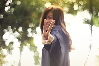 A joyful woman showing a peace sign with a blurred nature background. HD wallpaper