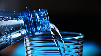 Close-up of sparkling water being poured from a bottle into a glass with bubbles visible. HD wallpaper