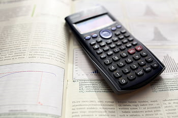 A graphing calculator rests on an open mathematics book with graphs and equations. HD wallpaper