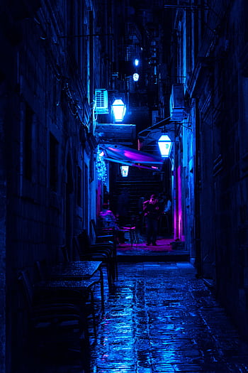 Atmospheric night scene of a city alley illuminated by vibrant blue lights with reflections on the wet ground. HD phone wallpaper