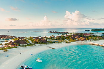 A stunning aerial view of a tropical Maldives beach with clear turquoise waters and resorts along the shore. HD wallpaper