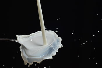 Capturing a dynamic splash of milk on a spoon in mid-air with dark background. HD wallpaper