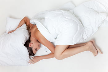 A serene of a woman sleeping comfortably wrapped in a white duvet on a plain bed. HD wallpaper