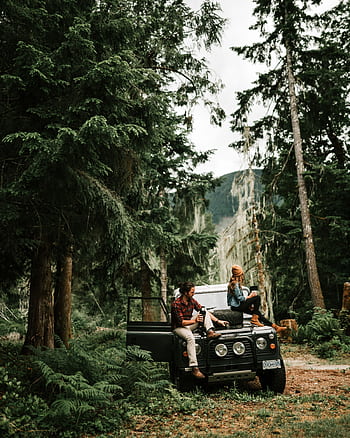 A couple sits on a classic off-road vehicle immersed in a tranquil forest setting, enjoying nature. HD phone wallpaper