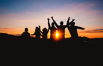 Group of friends silhouetted against a vibrant sunset sky, celebrating together outdoors. HD wallpaper